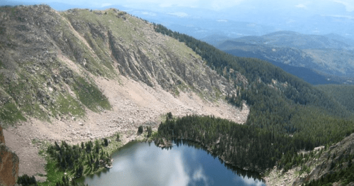 A scenic view of a mountain landscape with a serene lake surrounded by lush greenery and rocky terrain.