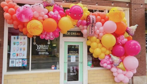 Colorful balloon arch in pink, orange, and yellow decorates the entrance of Loblolly Ice Cream shop.