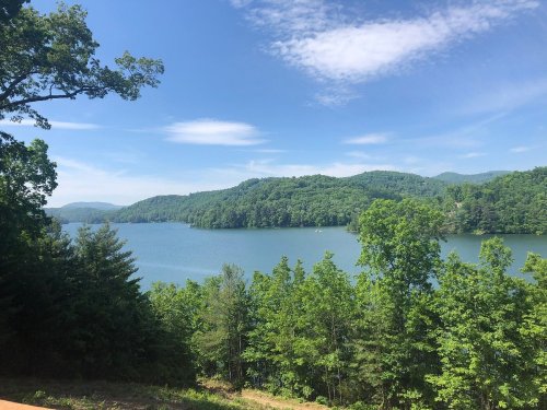 A serene lake surrounded by lush green hills and trees under a clear blue sky.