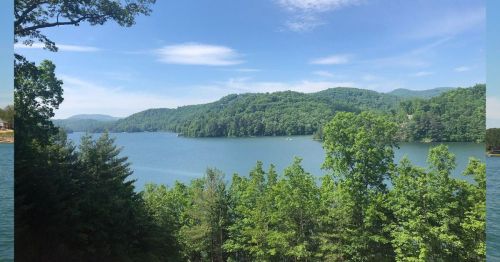 A serene lake surrounded by lush green hills and trees under a clear blue sky.
