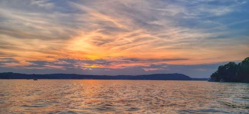 A serene sunset over a lake, with colorful clouds reflecting on the water and distant hills in the background.