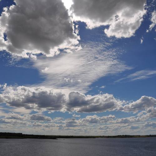 A scenic sky filled with fluffy clouds and wispy patterns, reflecting over a calm body of water.