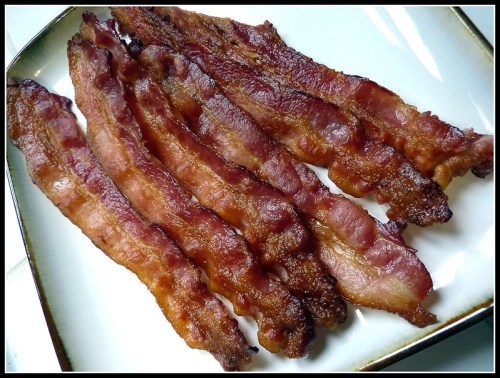 A plate of crispy, cooked bacon strips arranged neatly.