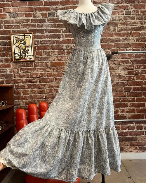 A floral-patterned dress with ruffled sleeves displayed on a mannequin against a brick wall.