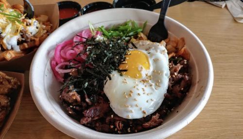 A bowl of rice topped with marinated meat, a fried egg, pickled vegetables, green onions, and seaweed.