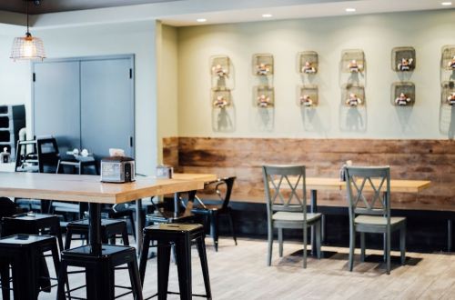 A modern café interior with wooden tables, black chairs, and decorative wall displays in a light green setting.