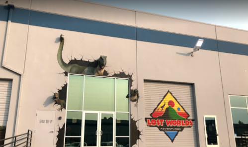 A mural of a dinosaur breaking through a wall at the entrance of Lost Worlds Adventures.