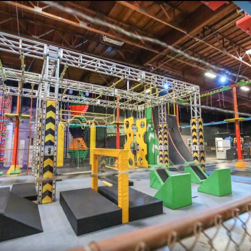 An indoor obstacle course featuring climbing walls, balance beams, and various colorful structures for physical activity.