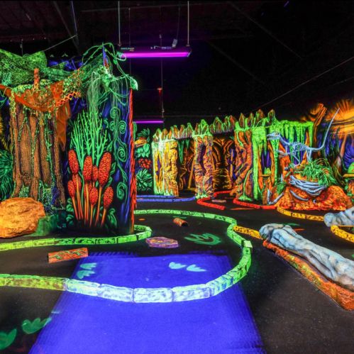 A vibrant, neon-lit mini-golf course featuring jungle-themed decorations and winding paths.
