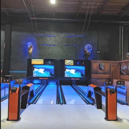 A bowling alley with two lanes, illuminated by blue lights and featuring screens at the end of each lane.