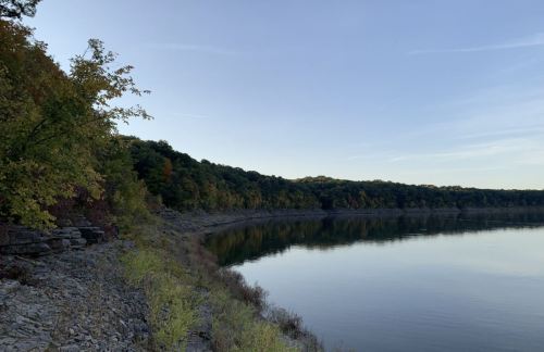 A calm lake surrounded by trees with autumn foliage, reflecting the clear sky at dusk.