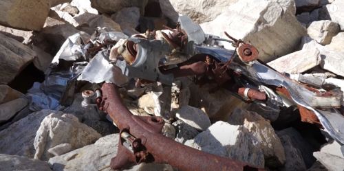 A pile of rocks with scattered metal debris, including rusted and crumpled pieces of machinery.