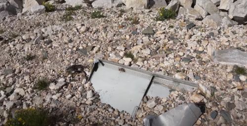 A piece of metal debris lies among rocks and gravel in a rugged outdoor setting.