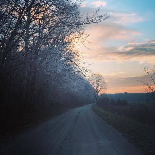 A winding road lined with frosty trees under a colorful sunrise sky.