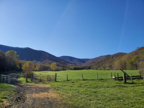 A serene landscape featuring a green field, wooden fences, and mountains under a clear blue sky.
