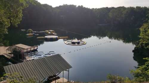 A serene lake with inflatable water toys, surrounded by trees and a wooden dock.