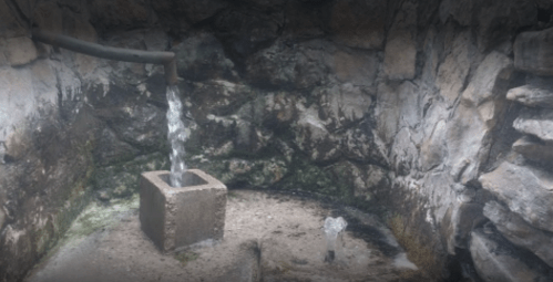 A stone well with flowing water, surrounded by rough, dark rock walls.