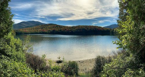 A serene lake surrounded by mountains and colorful autumn foliage under a blue sky with wispy clouds.