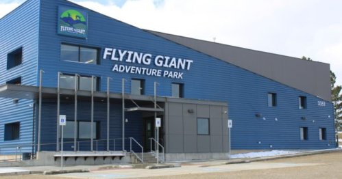 Blue building with "Flying Giant Adventure Park" sign, featuring large windows and a ramp entrance.