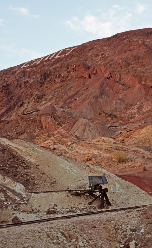 A desolate landscape with colorful rocky hills and an old mining cart on tracks in the foreground.
