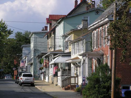 A quiet street lined with colorful houses, some displaying American flags, under a partly cloudy sky.
