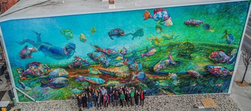 A vibrant mural depicting underwater life with colorful fish and a diver, alongside a group of people posing below it.