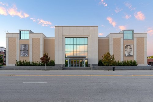 Modern building with large glass windows, featuring two portraits on the exterior and a clear blue sky in the background.