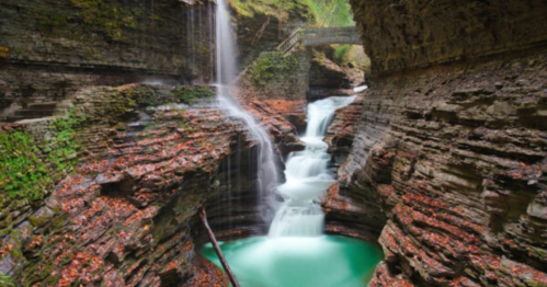A serene waterfall cascades into a turquoise pool, surrounded by rocky cliffs and lush greenery.