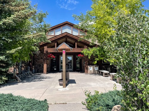 A rustic building surrounded by trees and flowers, featuring a large entrance and a clear blue sky.
