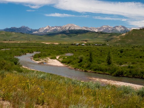 A serene landscape featuring a winding river, lush greenery, and mountains under a clear blue sky.