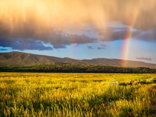 A vibrant landscape featuring green fields, distant mountains, and a rainbow under a dramatic sky.