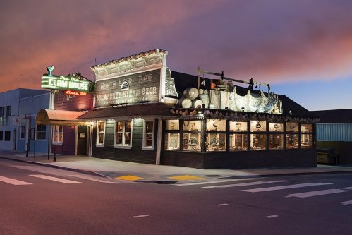 A charming restaurant with festive decorations, illuminated sign, and a colorful sunset sky in the background.
