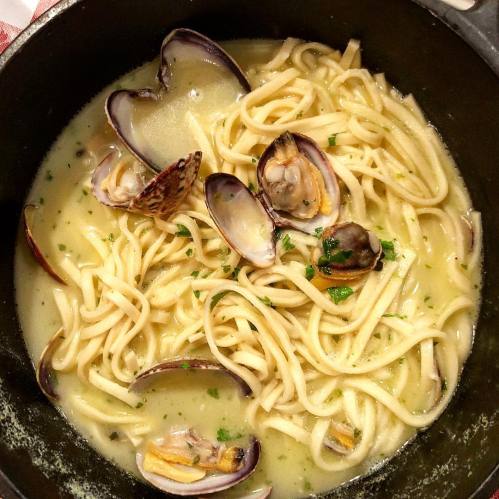 A bowl of linguine pasta with clams in a creamy sauce, garnished with parsley.