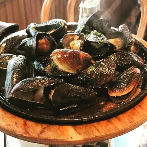 A wooden platter filled with steamed mussels, garnished with herbs and spices, steaming in a cozy setting.