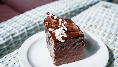 A slice of chocolate cake topped with chocolate shavings and striped chocolate sticks on a white plate.