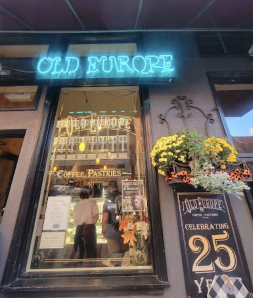 A storefront with a neon sign reading "Old Europe," featuring flowers and a celebration of 25 years.