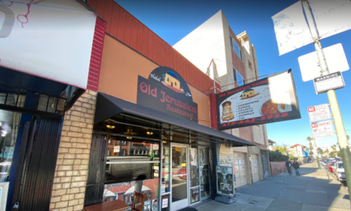 Exterior of Old Jerusalem Restaurant, featuring a sign and large windows, located on a city street.