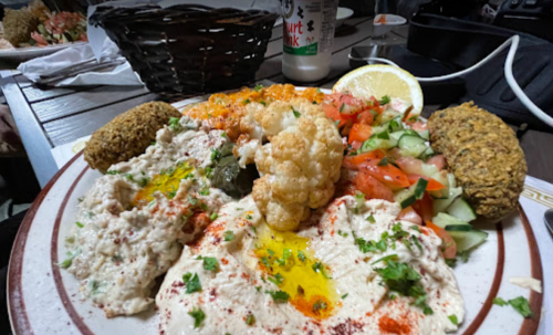 A colorful plate of hummus, falafel, roasted cauliflower, salad, and a lemon wedge, garnished with herbs and spices.