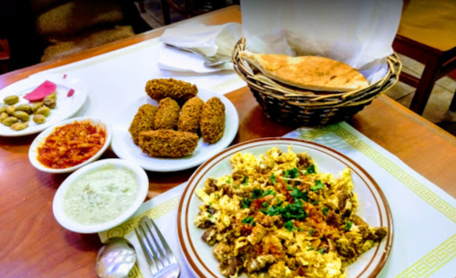 A plate of scrambled eggs with herbs, served with falafel, bread, olives, and dips on a wooden table.