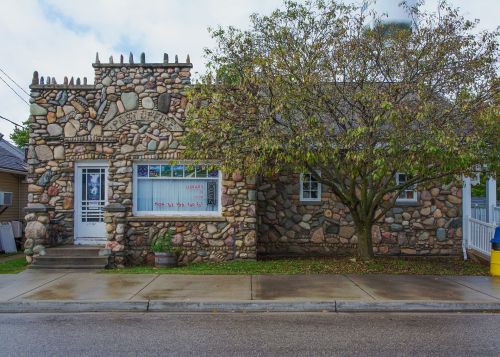 A unique stone building with a decorative facade and a tree in front, located on a quiet street.