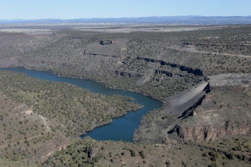 Aerial view of a winding river surrounded by rocky cliffs and green vegetation in a vast landscape.