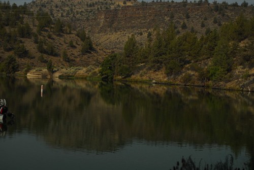 A serene river scene reflecting trees and hills, with calm water and a hint of a boat in the foreground.