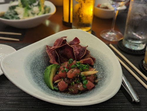 A plate of diced tuna with green onions, served with purple potato chips and avocado slices.