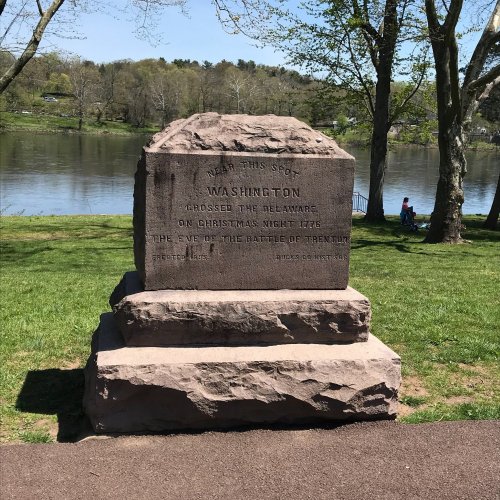A stone monument commemorating George Washington's crossing of the Delaware River, with a scenic river view in the background.