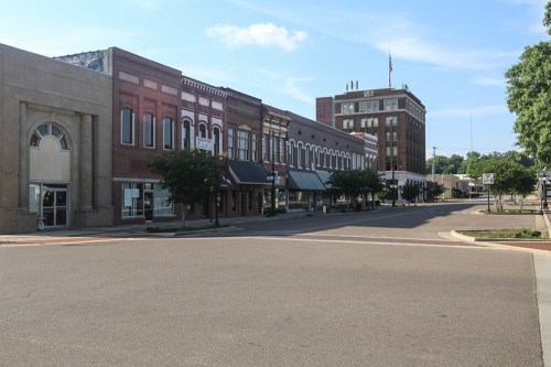 A quiet street scene featuring historic brick buildings and a tall structure in the background under a clear blue sky.