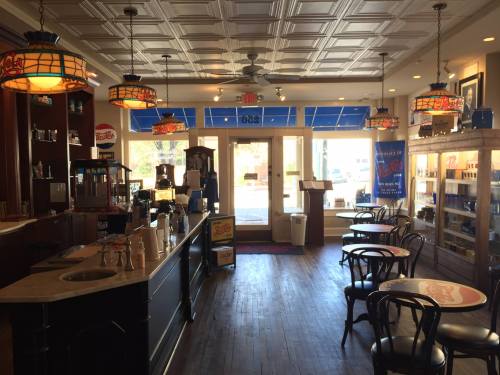 A cozy café interior with wooden floors, tables, and vintage lighting, featuring a counter and large windows.