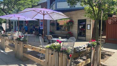 Outdoor café with purple umbrellas, wooden barriers, and flower planters, set in a lively street scene.