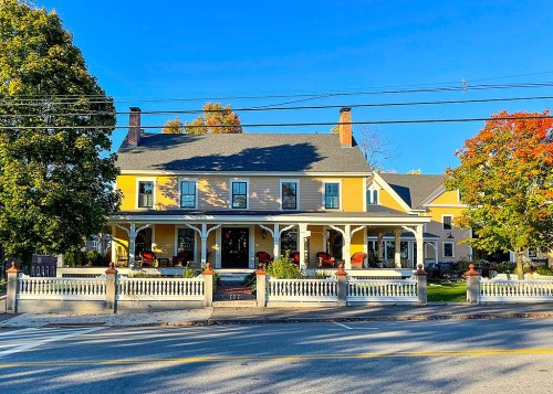 A charming yellow house with a porch, surrounded by trees and colorful autumn foliage, viewed from the street.