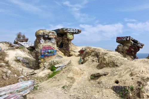 Colorful graffiti covers rocky formations on a sandy landscape under a blue sky.