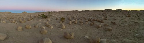 Panoramic view of a desert landscape with round stone formations and a colorful sky at dusk.